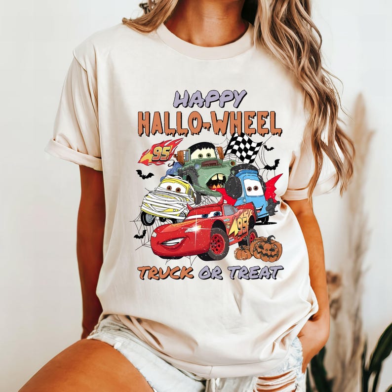May include: A beige t-shirt with a graphic print of cartoon cars and the text "Happy Hallo-Wheel Truck or Treat".