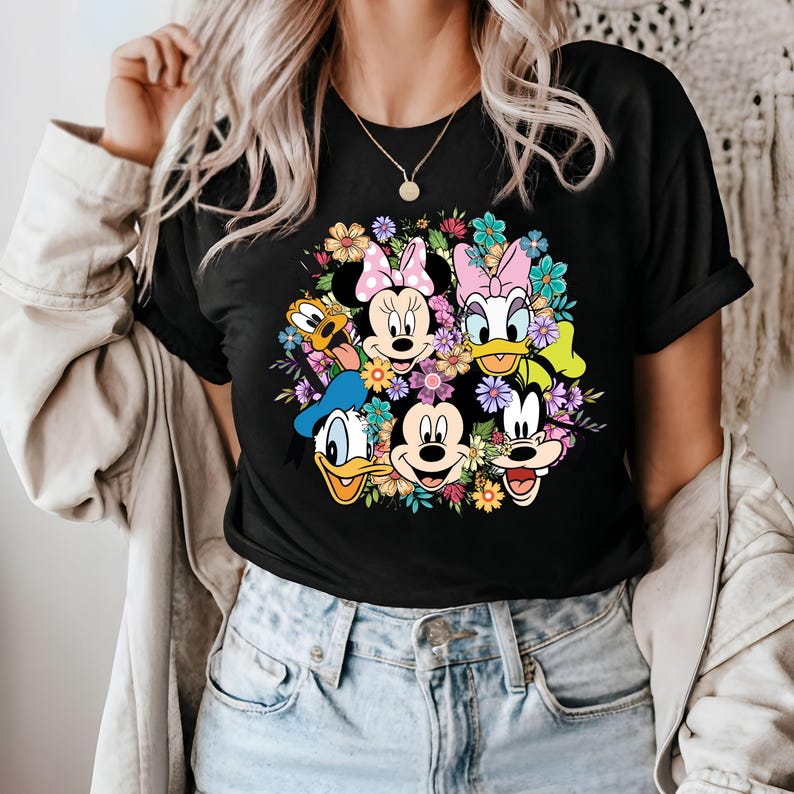 May include: Black t-shirt with a colorful graphic print of Mickey Mouse and friends surrounded by flowers.