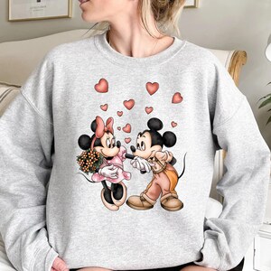 May include: A gray sweatshirt with a graphic print of Mickey Mouse and Minnie Mouse holding hands with hearts floating around them.