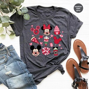 May include: A heather dark grey t-shirt with a graphic print of Mickey Mouse and Minnie Mouse with hearts, pizza, ice cream, and other Valentine's Day themed items.