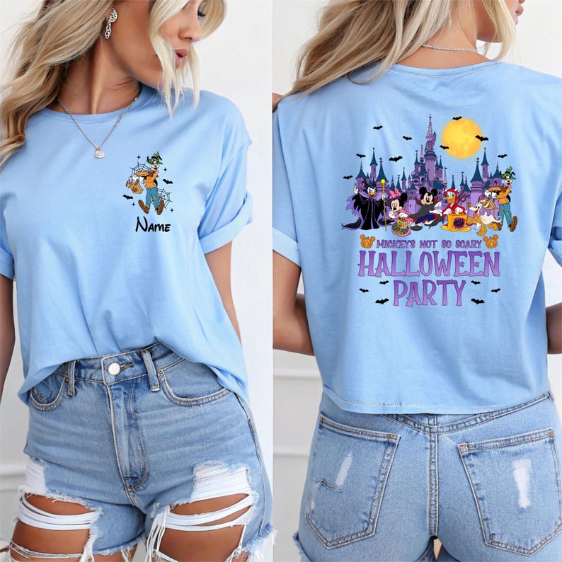 May include: Light blue t-shirt featuring a Halloween-themed graphic on the front and back. The front displays a cartoon character with a pumpkin and the word "Name". The back showcases a castle, characters, and the text "Mickey's Not So Scary Halloween Party".