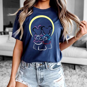 Puede incluir: Camiseta azul marino con una ilustraci&oacute;n de dibujos animados de dos personajes de rat&oacute;n abraz&aacute;ndose, sobre un c&iacute;rculo amarillo. El dise&ntilde;o incluye acentos rosas, azules y rojos. La camiseta es de cuello redondo y manga corta.