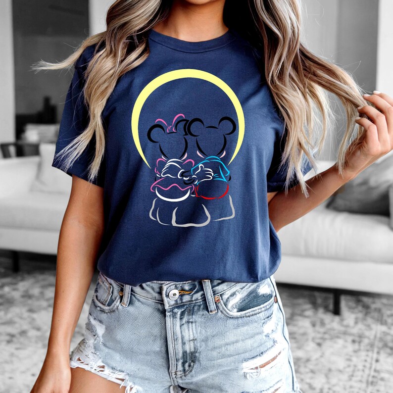 Puede incluir: Camiseta azul marino con una ilustraci&oacute;n de dibujos animados de dos personajes de rat&oacute;n abraz&aacute;ndose, sobre un c&iacute;rculo amarillo. El dise&ntilde;o incluye acentos rosas, azules y rojos. La camiseta es de cuello redondo y manga corta.