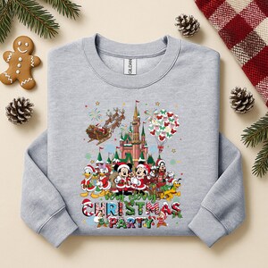 May include: A light gray sweatshirt featuring a colorful graphic of Disney characters in Christmas attire in front of a castle. The text "Very Merry Christmas Party" is displayed below the characters. Festive holiday apparel.