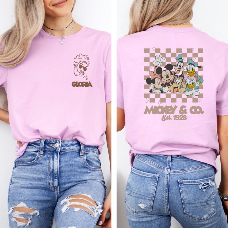 May include: A light pink t-shirt featuring a front graphic of a cartoon character with sunglasses and the name "Gloria". The back of the shirt displays a group of cartoon characters with the text "Mickey & Co. Est. 1928" on a checkered background.