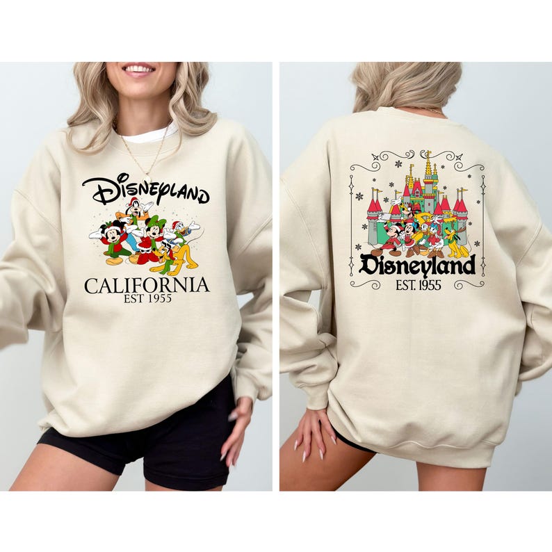 May include: Beige Disneyland sweatshirt with a front graphic of Disney characters and the text "Disneyland California EST 1955." The back features a castle graphic and the text "Disneyland EST 1955."