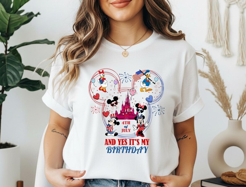 May include: White t-shirt featuring a Mickey Mouse design with patriotic elements. The design includes Mickey and Minnie Mouse, Donald and Daisy Duck, a castle, fireworks, and the text "4th of July AND YES IT'S MY BIRTHDAY".