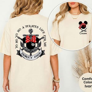 May include: Ivory-colored t-shirt with a pirate-themed design. The back features an anchor, Minnie Mouse bow, and the text "YO HO YO HO A PIRATES LIFE FOR ME DISNEY 2026." The front has a Mickey Mouse head with a bandana and crossed swords.