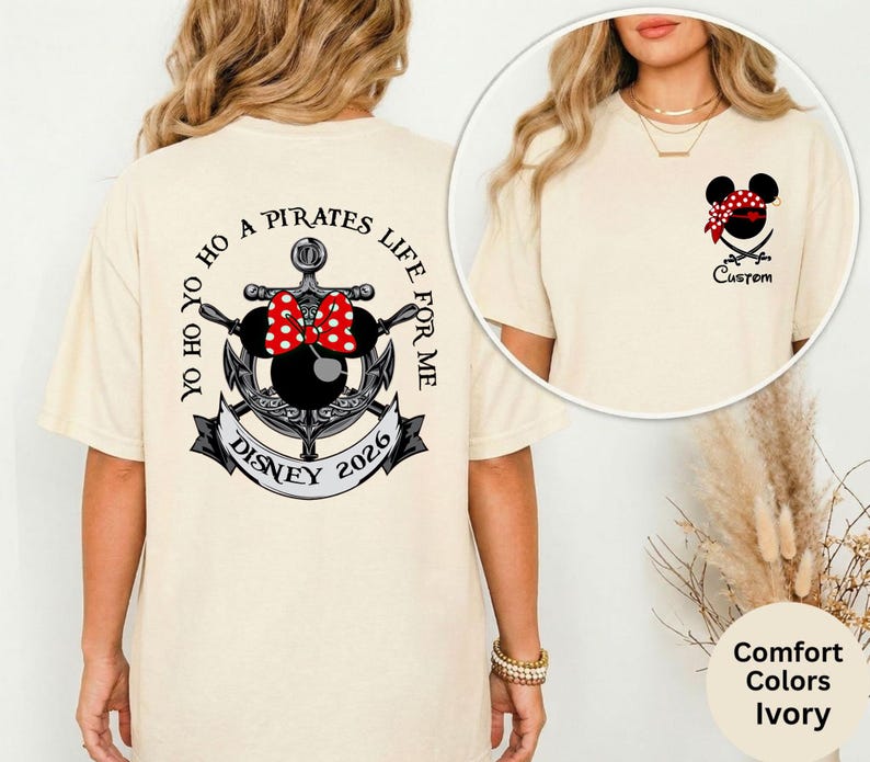 May include: Ivory-colored t-shirt with a pirate-themed design. The back features an anchor, Minnie Mouse bow, and the text "YO HO YO HO A PIRATES LIFE FOR ME DISNEY 2026." The front has a Mickey Mouse head with a bandana and crossed swords.