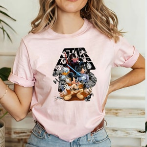May include: Pink t-shirt with a black and white graphic of Mickey Mouse, Donald Duck, and Minnie Mouse dressed as Star Wars characters. The graphic includes the text "Star Wars" in a black triangle.