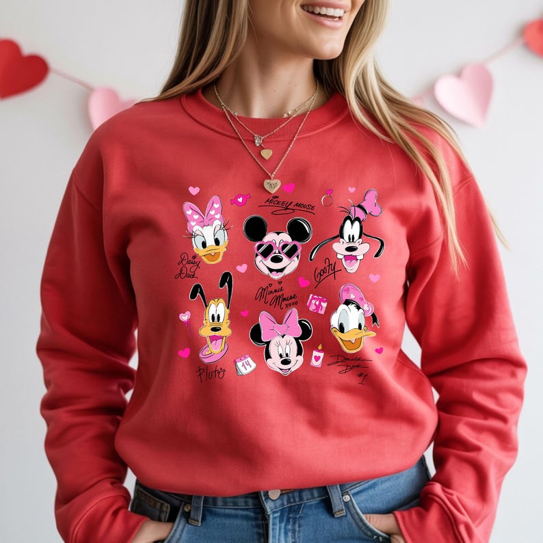 May include: Red sweatshirt featuring cartoon characters Daisy Duck, Mickey Mouse, Goofy, Pluto, Minnie Mouse, and Donald Duck. The design includes pink hearts and text. A Valentine's Day themed apparel item.
