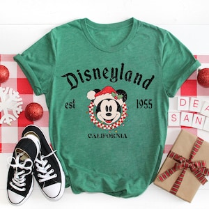 Puede incluir: Camiseta verde con un logotipo vintage de Disneyland con Mickey Mouse con un gorro de Pap&aacute; Noel. El texto dice "Disneyland est 1955 California".