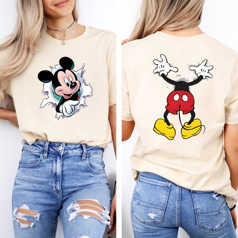 Puede incluir: Camiseta beige con un gr&aacute;fico de Mickey Mouse. La parte delantera de la camiseta muestra a Mickey rompiendo un dise&ntilde;o rasgado, mientras que la parte trasera muestra la parte trasera de Mickey. La camiseta se usa con jeans azules.