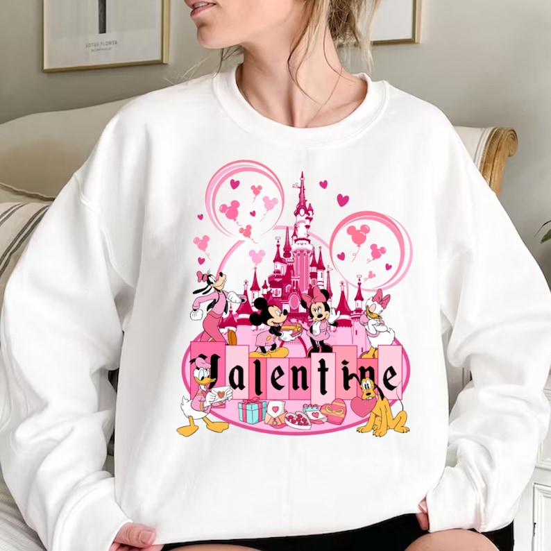 May include: White sweatshirt with a pink graphic of Mickey Mouse and friends in front of Sleeping Beauty's castle with the word "Valentine" printed below.