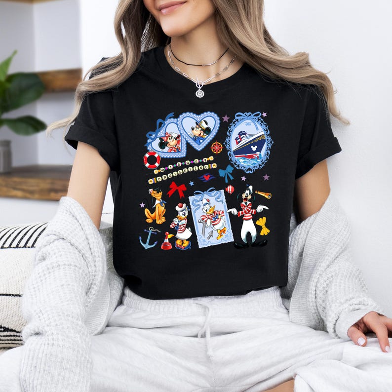 May include: Black t-shirt with a colorful graphic print featuring Mickey Mouse, Minnie Mouse, Donald Duck, Goofy, and a cruise ship. The graphic includes hearts, stars, and nautical elements.