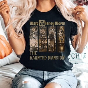 May include: A black t-shirt featuring a graphic of characters from the Haunted Mansion ride at Walt Disney World. The text "Walt Disney World" and "The Haunted Mansion" is printed on the shirt.