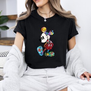 Puede incluir: Camiseta negra con un gr&aacute;fico de Mickey Mouse colorido. El gr&aacute;fico est&aacute; formado por varios personajes de Disney, entre ellos Simba, Ariel y Bella.