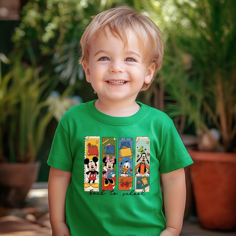 May include: A green t-shirt featuring Mickey Mouse, Minnie Mouse, Donald Duck, and Goofy. The design includes the words "back to school" and is displayed on a young child.