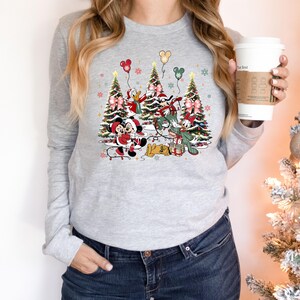 May include: A gray long-sleeved sweatshirt with a Christmas-themed design featuring Mickey Mouse, Minnie Mouse, Donald Duck, Goofy, and Pluto. The characters are standing in front of Christmas trees with presents and ornaments.