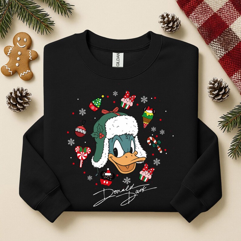 May include: Black sweatshirt featuring a graphic of Donald Duck wearing a green and white winter hat. The design includes Christmas-themed elements like ornaments, snowflakes, and candy canes. The words "Donald Duck" are written in a cursive font.