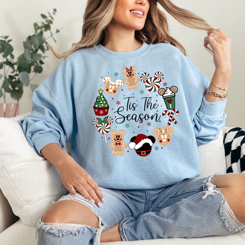 Peut inclure: Sweat-shirt bleu clair avec un motif de couronne de No&euml;l. La couronne comprend des bonhommes en pain d'&eacute;pices, des cannes en sucre, un sapin de No&euml;l et le texte "Tis The Season". Le motif est circulaire, parfait pour la saison des f&ecirc;tes.