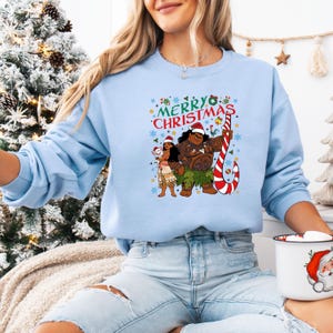 May include: Light blue sweatshirt with a graphic featuring characters and the text "Merry Christmas." The design includes a candy cane and festive elements. The sweatshirt is a long-sleeved crew neck.
