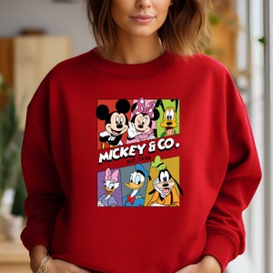 Pu&ograve; includere: Felpa rossa con una grafica colorata di Topolino, Minnie Mouse, Paperino, Pippo e Pluto. La grafica include il testo "Mickey & Co. Est. 1928".
