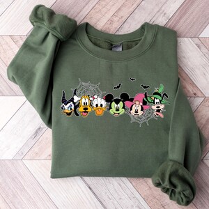Pu&ograve; includere: Felpa verde con un design a tema di Halloween con Topolino, Minnie Mouse, Paperino, Pippo e un personaggio spettrale. Il design include pipistrelli e ragnatele.