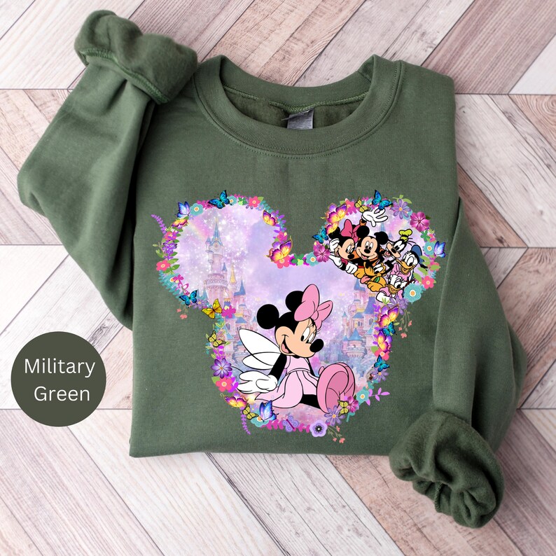 May include: A green sweatshirt with a floral Mickey Mouse design. The design features Mickey Mouse and Minnie Mouse with a pink castle in the background.