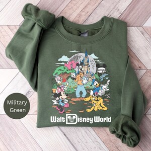 May include: A green sweatshirt with a graphic print of Mickey Mouse and friends at Walt Disney World. The sweatshirt has a crew neck and long sleeves.