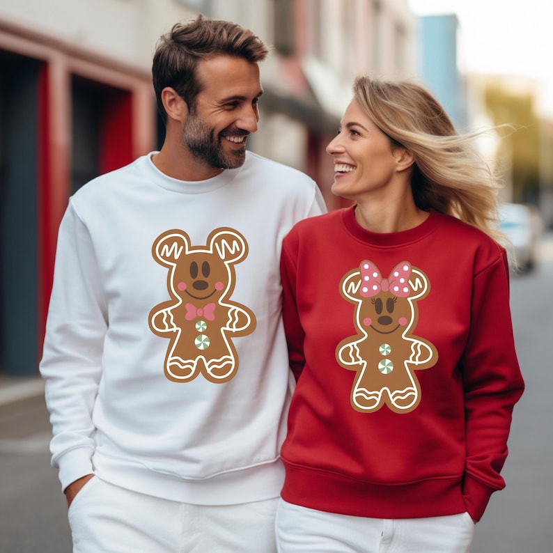 May include: A white sweatshirt with a gingerbread Mickey Mouse design and a red sweatshirt with a gingerbread Minnie Mouse design. The couple are wearing matching sweatshirts.