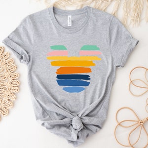 May include: A gray t-shirt with a colorful Mickey Mouse silhouette design. The silhouette is made up of horizontal stripes in shades of blue, green, yellow, orange, and pink.