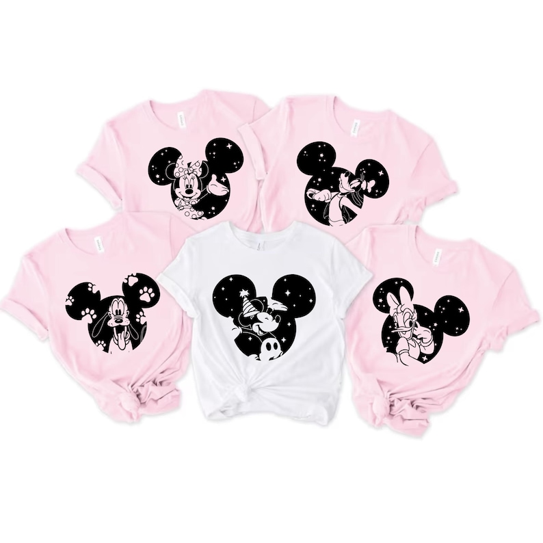 May include: Five short-sleeved t-shirts in pink and white. Each shirt features a black Mickey Mouse silhouette with different character designs. The designs include Minnie Mouse, Goofy, Mickey Mouse, and Donald Duck.