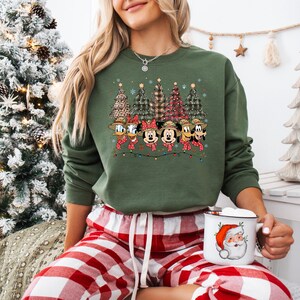 May include: Green crewneck sweatshirt featuring a Christmas design with cartoon characters and Christmas trees. The graphic includes Donald Duck, Minnie Mouse, Mickey Mouse, Goofy, and Pluto. The sweatshirt is paired with red and white plaid pajama pants.
