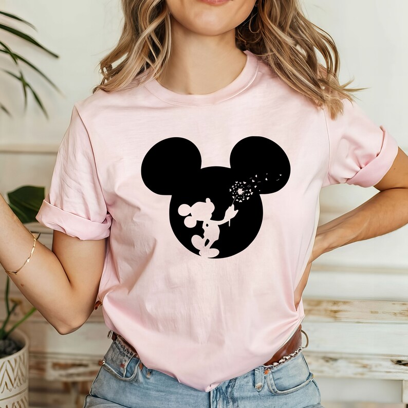 May include: Pink t-shirt with a black silhouette of Mickey Mouse blowing on a dandelion. The silhouette is inside a black outline of Mickey Mouse's head.