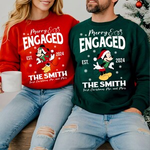 Puede incluir: Una pareja vistiendo su&eacute;teres navide&ntilde;os a juego en rojo y verde con Mickey Mouse y el texto "Merry & Engaged" y "The Smith First Christmas Mr. and Mrs. 2024".