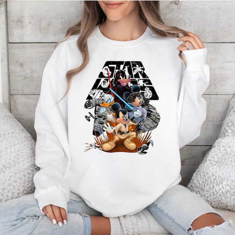 May include: White sweatshirt with a black and white graphic of Mickey Mouse, Donald Duck, and Goofy dressed as Star Wars characters. The graphic includes the Star Wars logo and a lightsaber.