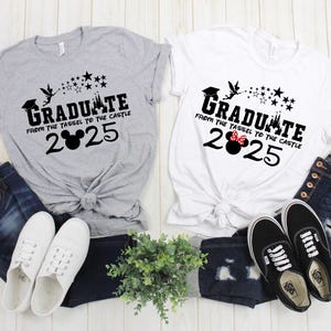 以下が含まれることがあります： 黒と白のグラフィックデザインが施されたグレーと白のTシャツ2枚。グラフィックデザインには、シンデレラ城のシルエット、星、そして「Graduate from the tassel to the castle 2025」というテキストが描かれています。1枚のシャツには黒いミッキーマウスのシルエット、もう1枚には赤いミニーマウスのシルエットが描かれています。