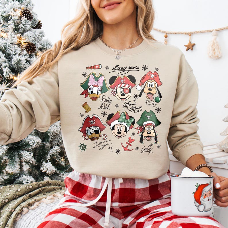 May include: Beige sweatshirt featuring a graphic of Mickey Mouse and friends in pirate attire. The design includes images of Donald Duck, Daisy Duck, Minnie Mouse, Pluto, and Goofy, with the words "Mickey Mouse" and character names.