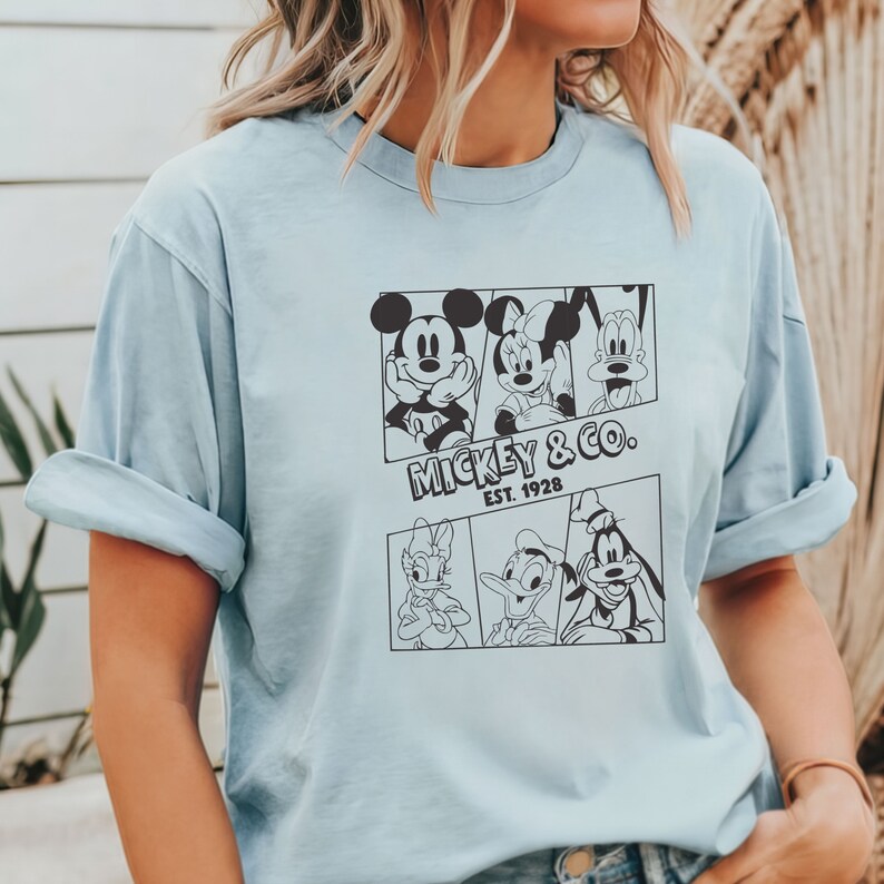 K&ouml;nnte beinhalten: Hellblaues T-Shirt mit einem schwarz-wei&szlig;en Grafikdruck von Mickey Mouse, Minnie Mouse, Donald Duck und Goofy. Die Grafik enth&auml;lt den Text "Mickey & Co. Est. 1928".