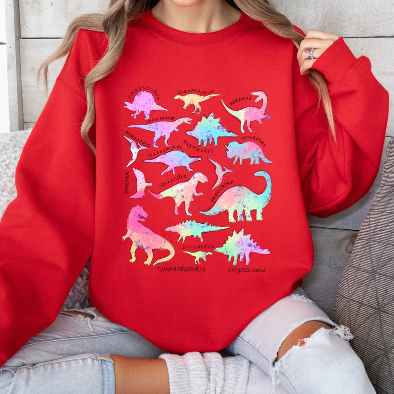 May include: Red sweatshirt with a rainbow-colored dinosaur graphic. The dinosaurs are labeled with their names, including Stegosaurus, Tyrannosaurus, Brachiosaurus, and Triceratops.