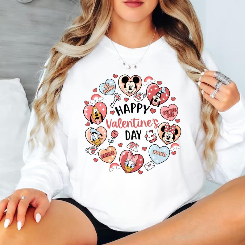 K&ouml;nnte beinhalten: Wei&szlig;es Sweatshirt mit einem Valentinstagsdesign. Das Design zeigt Zeichentrickfiguren, Herzen, Regenbogen und den Text "Happy Valentine's Day". Das Design ist in Rosa-, Rot- und Blaut&ouml;nen gehalten.