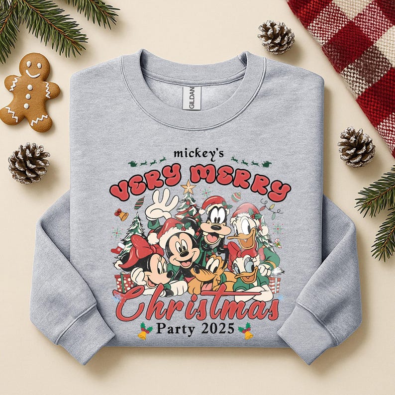 Puede incluir: Sudadera gris claro con un dise&ntilde;o festivo de Mickey Mouse y sus amigos con atuendos navide&ntilde;os. El dise&ntilde;o incluye el texto "mickey's VERY MERRY Christmas Party 2025" en rojo y verde. Prenda de tem&aacute;tica navide&ntilde;a.