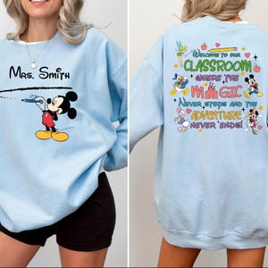 May include: Light blue sweatshirt with a Mickey Mouse design on the front and a Disney-themed quote on the back. The quote reads "Welcome to our classroom where the magic never stops and the adventure never ends".