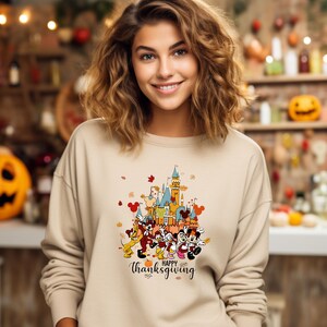 May include: A beige sweatshirt with a graphic print of Mickey Mouse and friends in front of a cartoon version of the Cinderella Castle. The graphic also includes the text "Happy Thanksgiving".