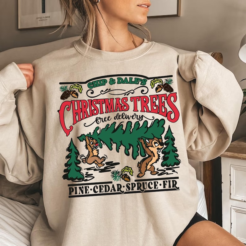 K&ouml;nnte beinhalten: Ein beiger Pullover mit einem Weihnachtsbaum-Motiv mit Chip und Chap. Der Text lautet "Chip & Dale's Christmas Trees, free delivery, Pine-Cedar-Spruce-Fir".