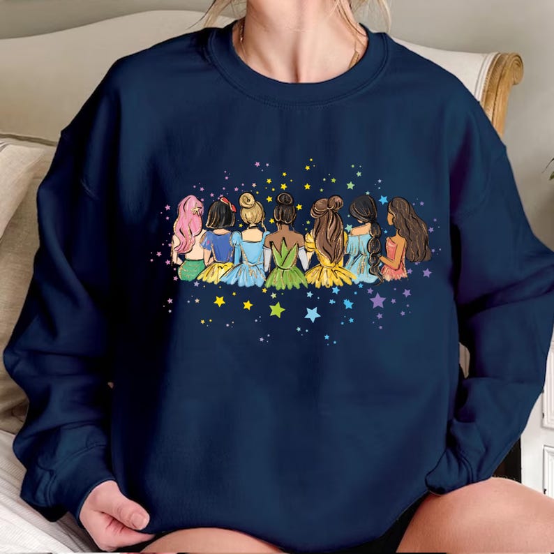 May include: A navy blue sweatshirt with a graphic of seven princesses standing back to back with their hair down. The princesses are wearing colorful dresses and are surrounded by stars.