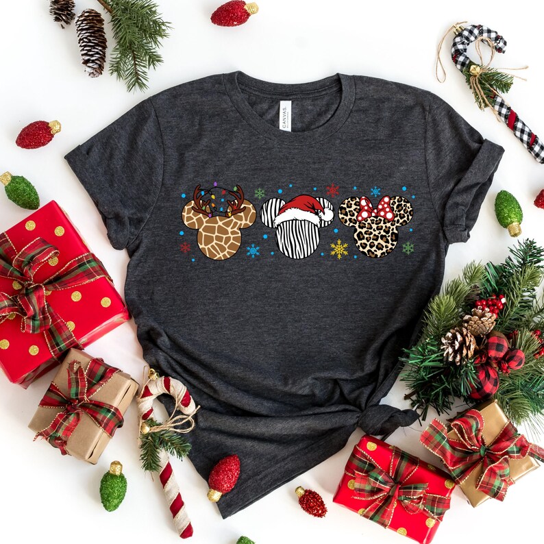 May include: A dark gray t-shirt with a Christmas-themed design featuring three cartoon animal heads. The heads are a reindeer with antlers and lights, a zebra wearing a Santa hat, and a leopard with a red bow. The design is centered on the shirt.