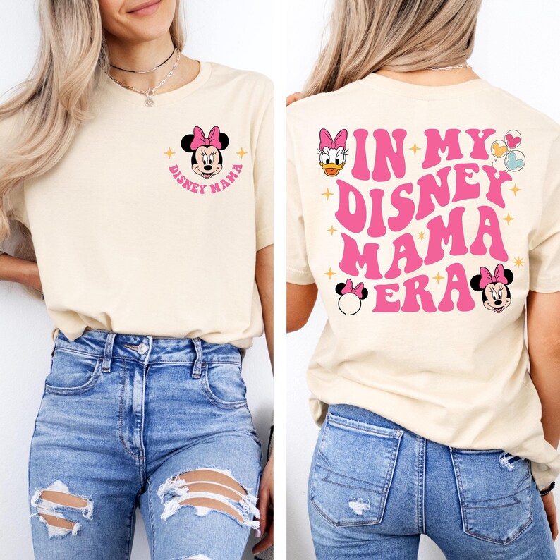 May include: A light beige t-shirt with a pink graphic that says "In My Disney Mama Era" with images of Mickey Mouse, Minnie Mouse, and Daisy Duck. The shirt is being modelled by a person wearing blue jeans.
