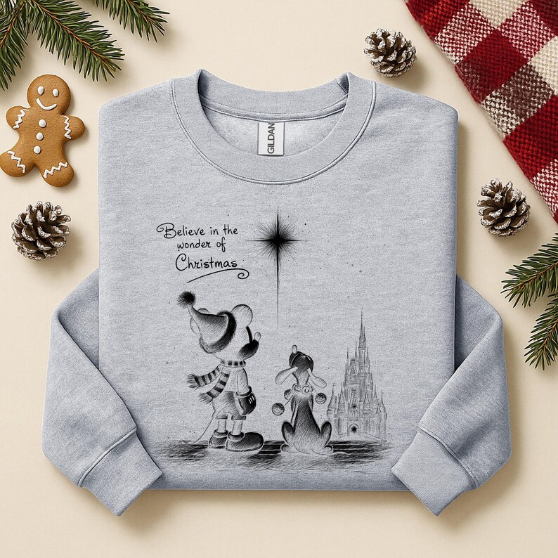 May include: A light gray sweatshirt featuring a black and white illustration of a cartoon mouse and dog looking at a star. The text "Believe in the wonder of Christmas" is above the characters. A gingerbread man and pinecones are in the background.